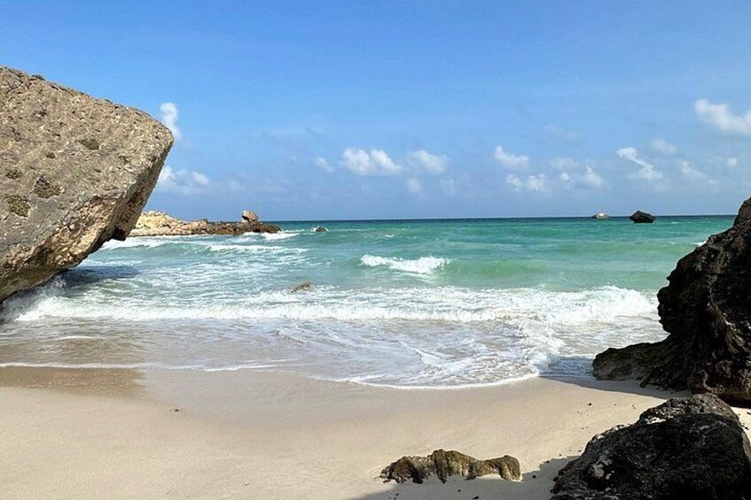 Een strand met helder turquoise water, een zandstrand en grote rotsen. 2