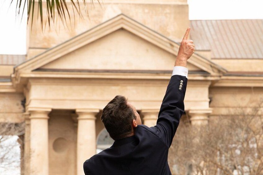 A person in a suit pointing upwards with a building in the background. 5