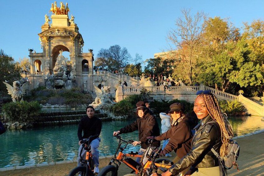 A group of people on bicycles near a historic fountain with a bridge in the background. 5