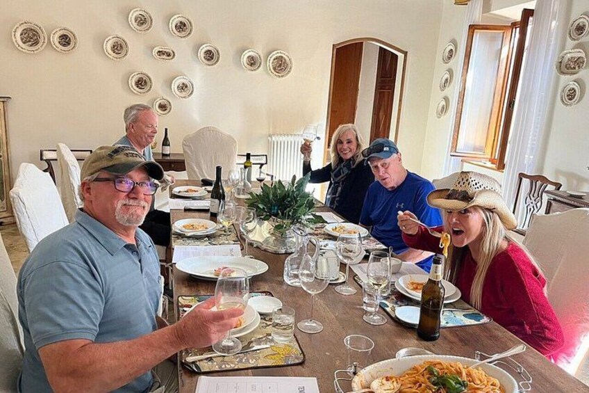 A group of people dining at a table with plates of food, wine glasses, and a bottle of wine. 1