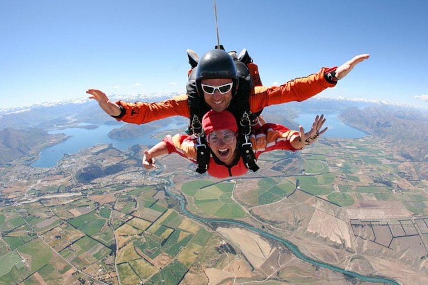 Two people skydiving with a mountainous landscape below. 2