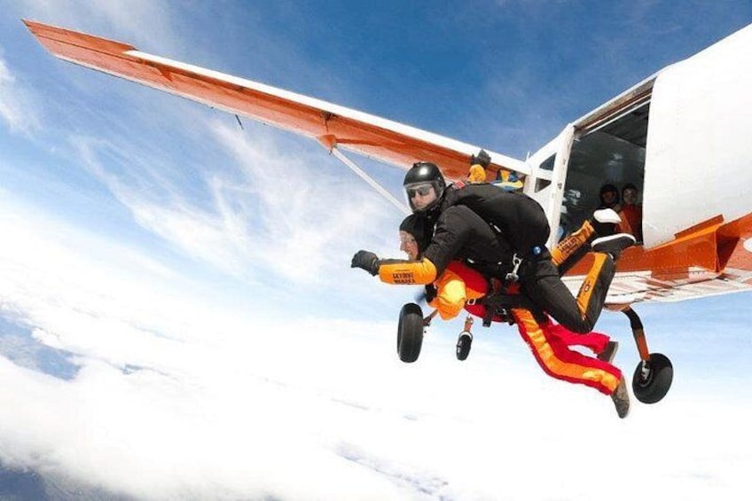 A person skydiving with a parachute, wearing a helmet and harness, and a small aircraft in the background. 4