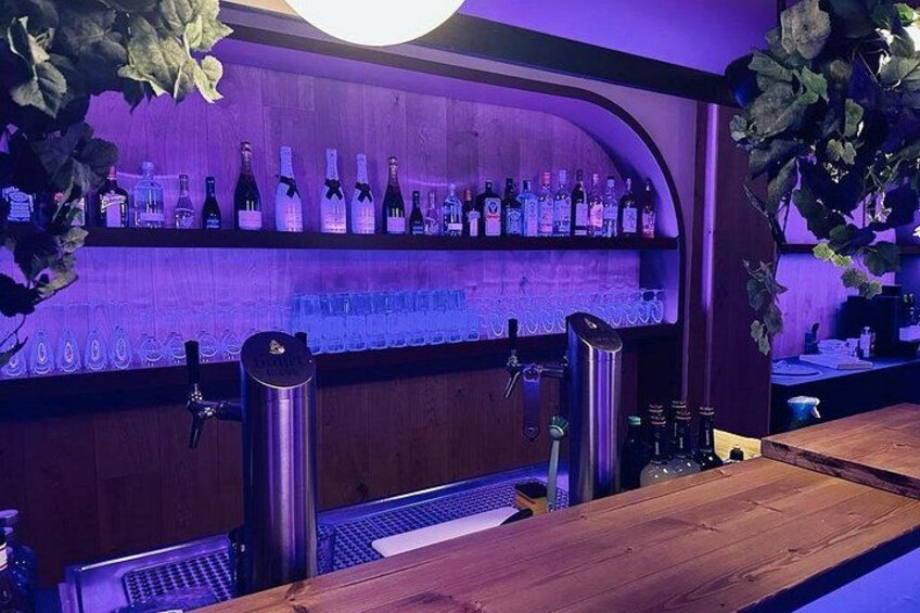 Un bar con estantes llenos de botellas, un grifo y una barra de madera. 2