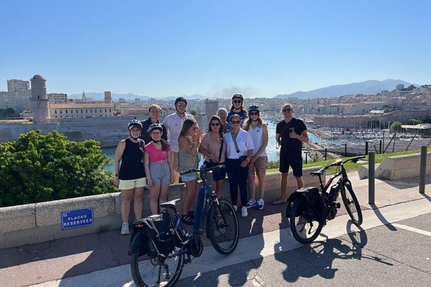 Un groupe de personnes posant sur une promenade en bord de mer, avec des vélos, et un fort historique en arrière-plan. 5