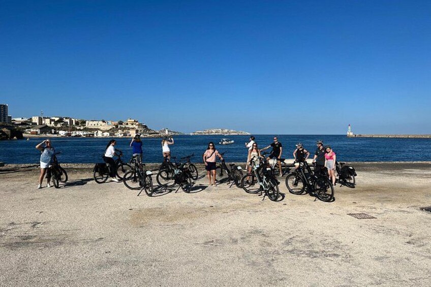 A group of people with bicycles by a coastal area with a lighthouse in the background. 3