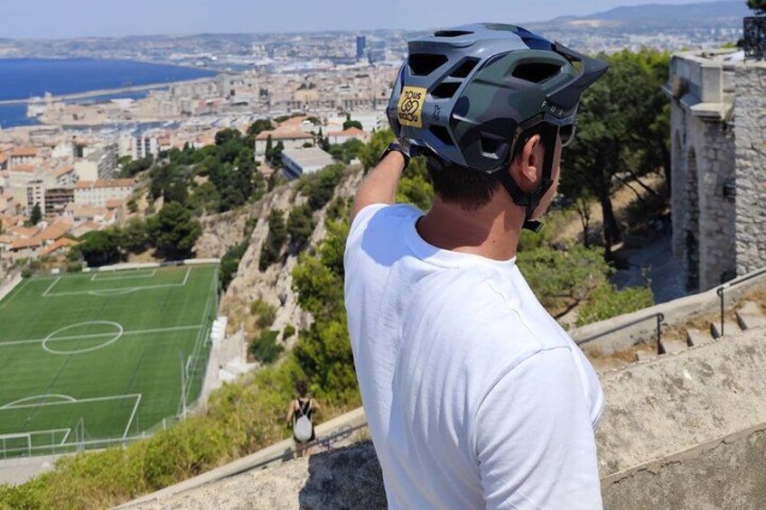 Une personne portant un casque et un t-shirt blanc, qui surplombe un paysage urbain avec un terrain de football. 2