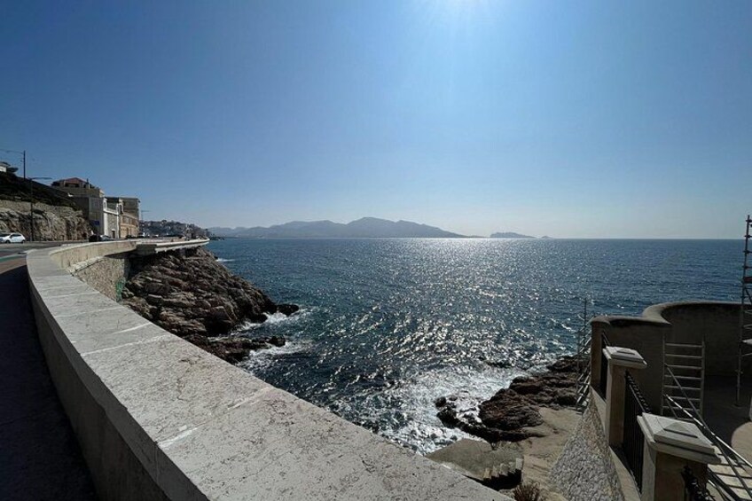 A coastal road with a sea view, rocky shoreline, and distant mountains. 4