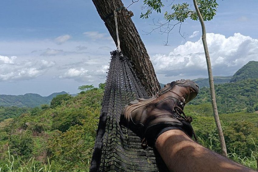 A person's leg resting on a hammock, surrounded by lush greenery and hills. 5