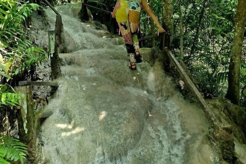 Une personne se promène sur un chemin de béton qui traverse une zone boisée, près d’une petite cascade. 1