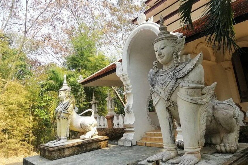 A temple with statues of a deity and a lion, surrounded by trees and a building with a red roof. 5