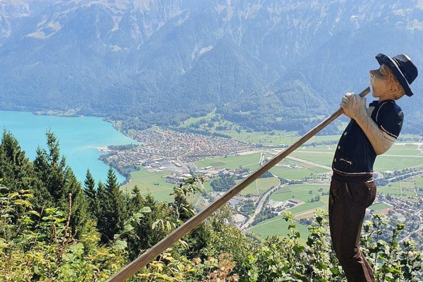 Eine Person steht auf einem Berg, hält einen langen Stock und blickt auf eine Stadt und einen See. 3