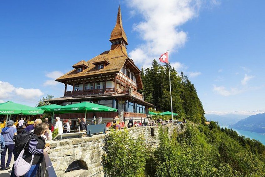 Ein traditionelles Holzgebäude mit einem steilen Dach, umgeben von üppigem Grün und einem klaren Himmel. 5