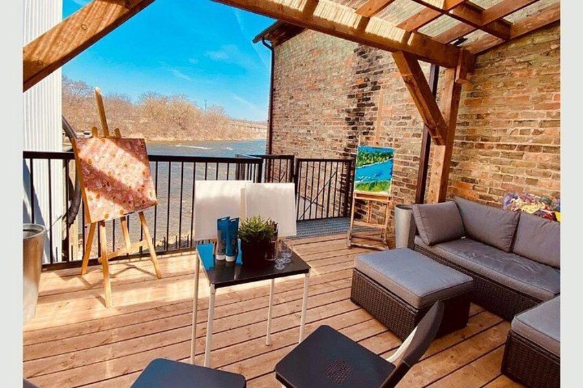 An outdoor deck with a wooden floor, a painting on an easel, a sofa, and a table with a plant. 4