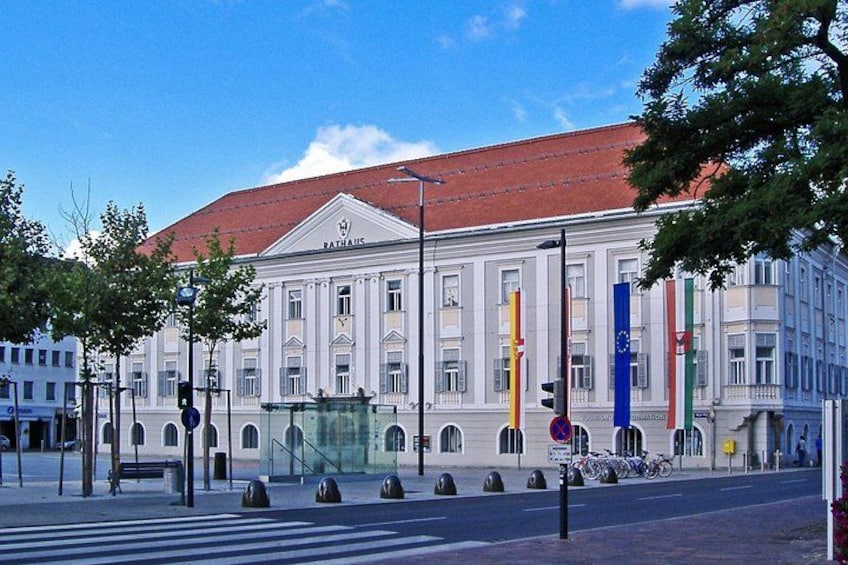 A large white building with columns, a red roof, and flags. 1
