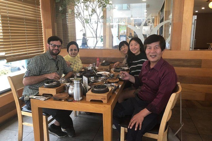 A group of people sitting at a wooden table with various dishes and a coffee pot. 4