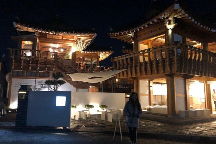 A traditional wooden building with a balcony, illuminated by lights at night. 2