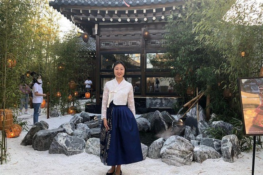 A person standing in a traditional Japanese garden with rocks, bamboo, and a wooden structure. 2