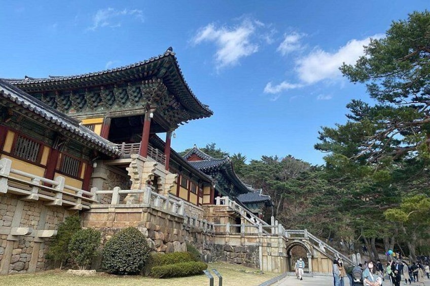 En traditionel koreansk bygning med et flisegulvt tag, stenvægge og en stentrappe, der fører op til den. 2