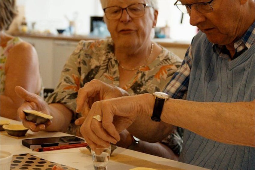 An elderly couple at a table with a smartphone, a glass, and a small container. 4