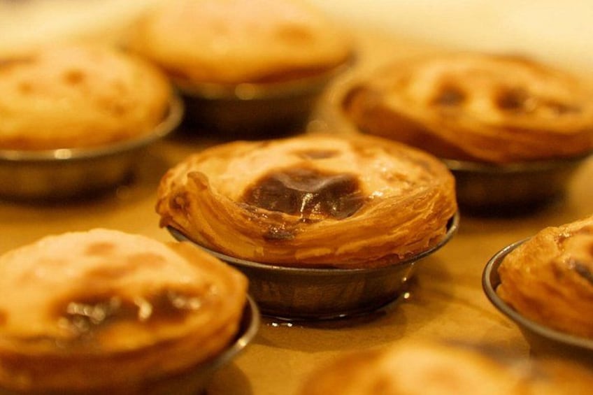A close-up of several custard tarts in individual metal cups. 1