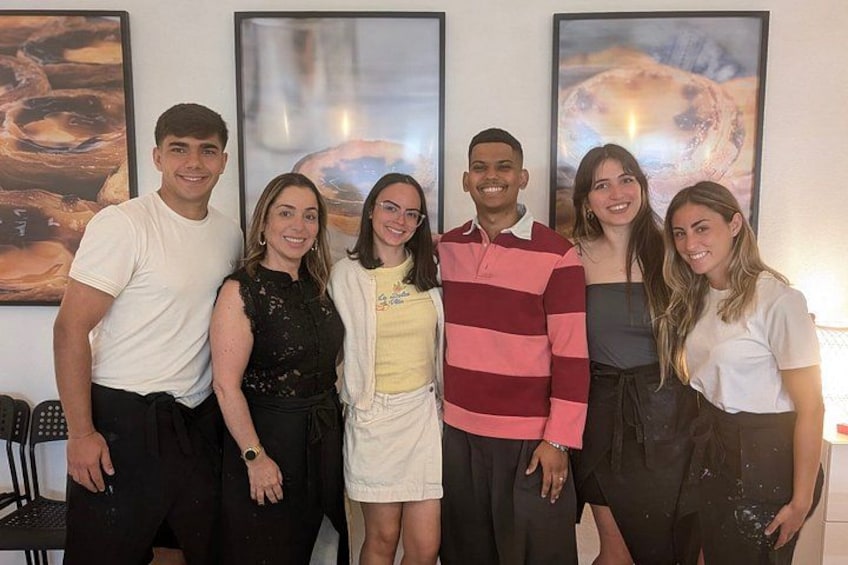 A group of people standing indoors with abstract paintings on the wall behind them. 2
