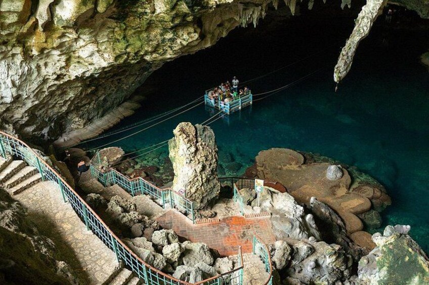 A cave with a rope bridge, clear blue water, and rocky formations. 1
