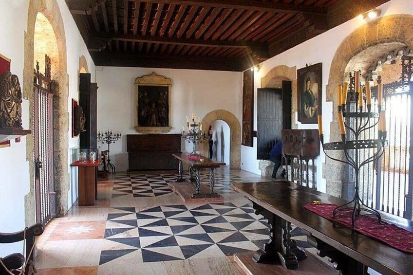 A room with a checkered floor, wooden beams, a table, and a painting on the wall. 5