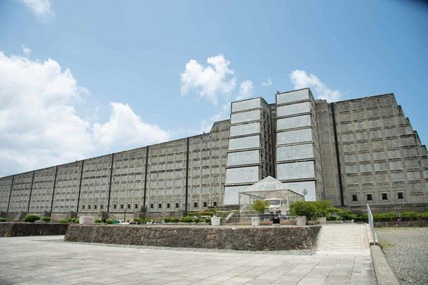 A large, rectangular building with a symmetrical facade, a central glass structure, and a paved area in front. 4
