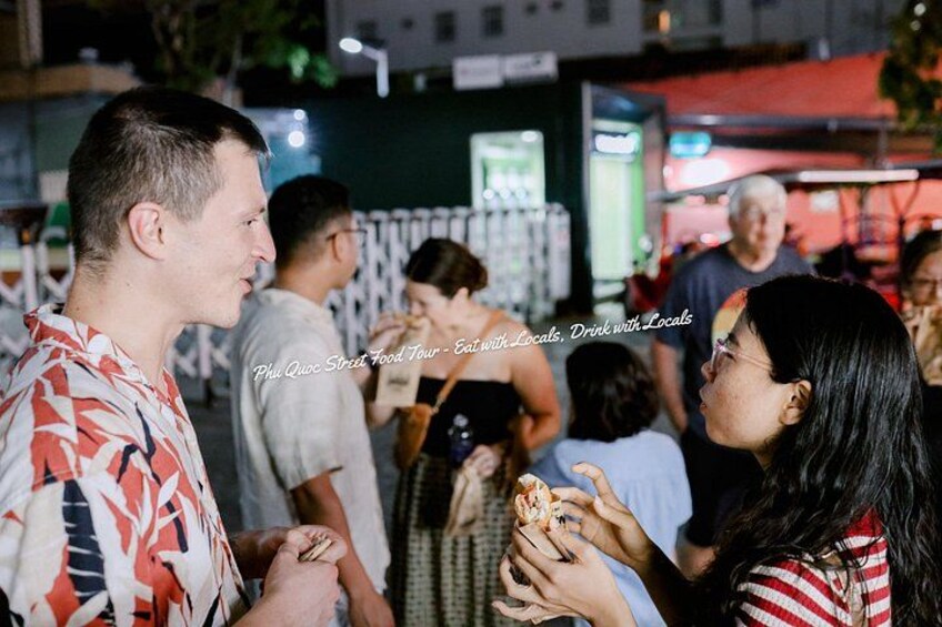 A group of people at an outdoor event, possibly a street food tour, with food being served. 1