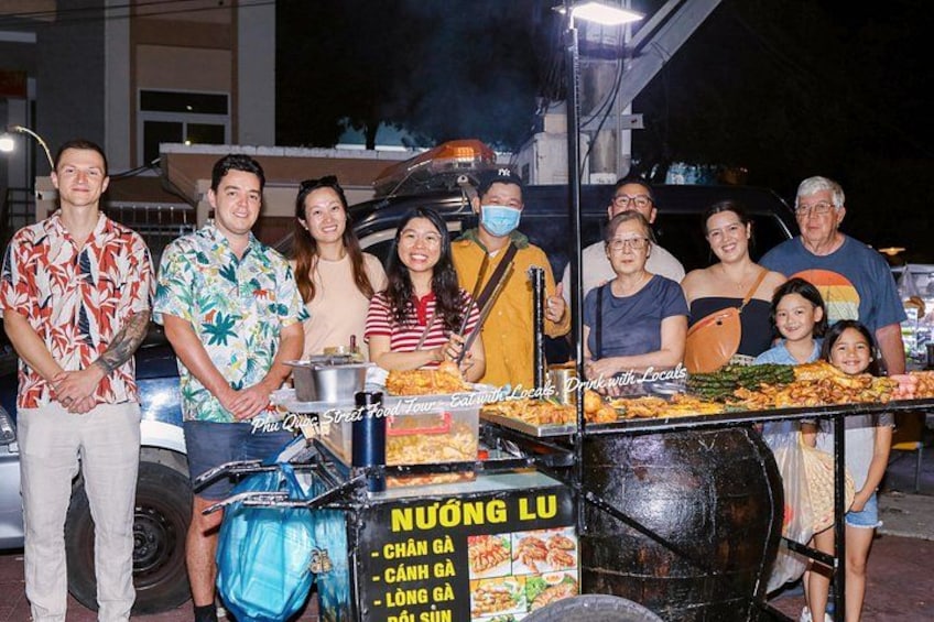 A group of people at a food stall with a large cooking pot and a sign that reads 'NUONG LU'. 5