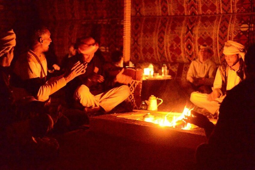 Un grupo de personas sentadas alrededor de una fogata en una habitación tenuemente iluminada con paredes decoradas. 2