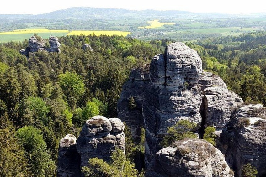 A landscape with prominent rock formations surrounded by dense forest and rolling hills in the background. 1