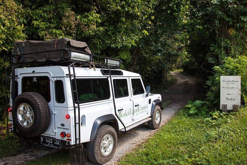 A white off-road vehicle parked on a dirt path surrounded by greenery. 1