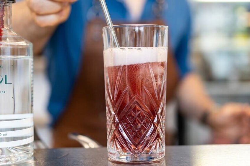 A glass of red beverage with a straw, a bottle of water, and a person in the background. 2