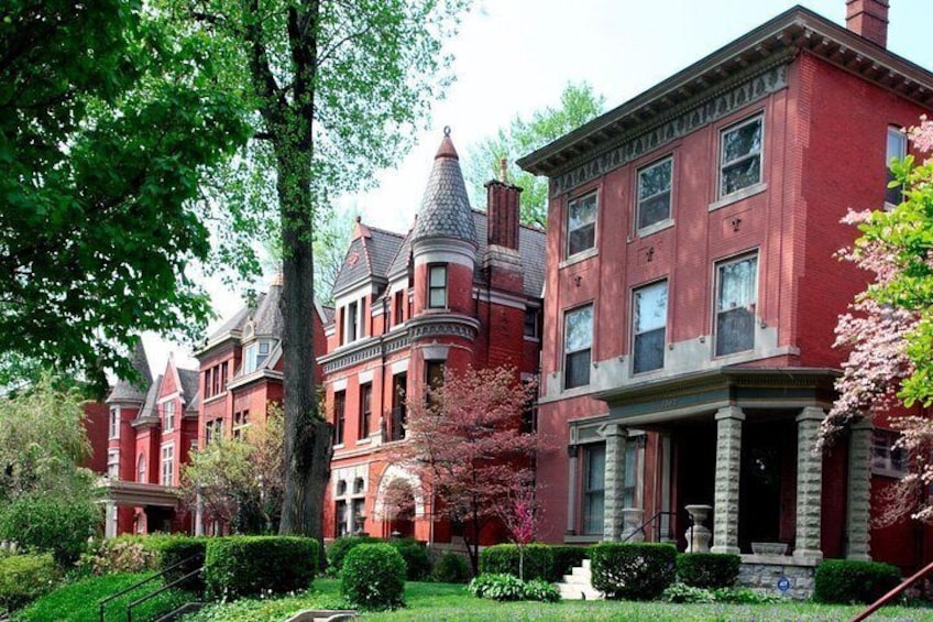 A red brick Victorian house with a turret and columns, surrounded by well-maintained gardens and trees. 4