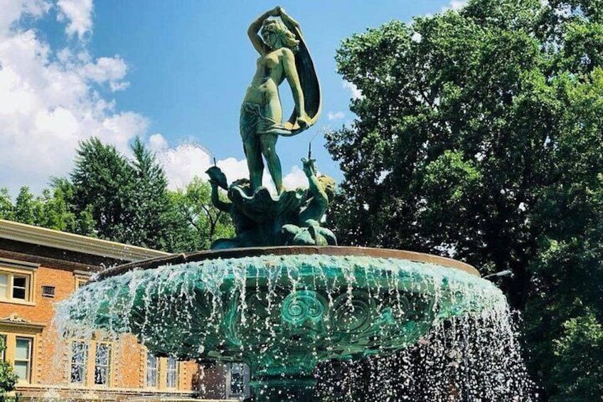 A fountain with a statue of a woman holding a fish, surrounded by water spray. 5