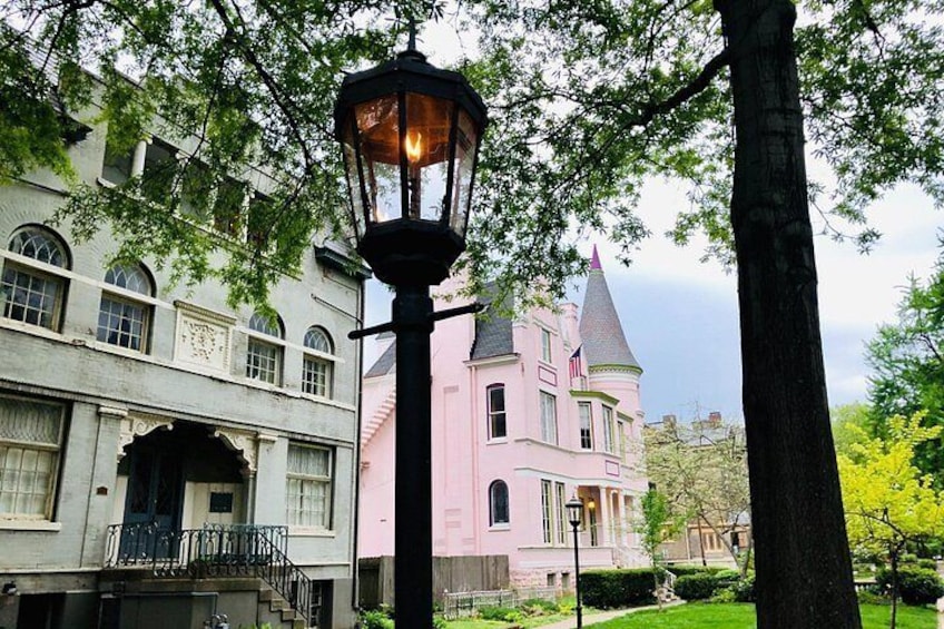 A pink building with a turret, a street lamp, and a tree. 2