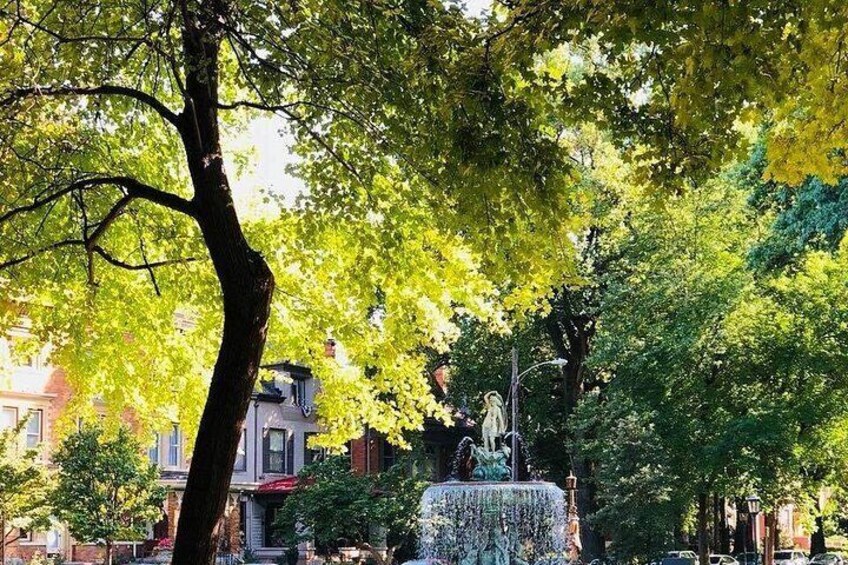 A park with a fountain, trees, and buildings in the background. 3