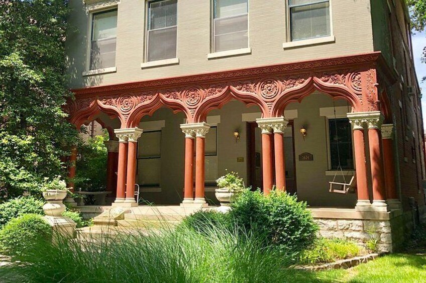 A two-story building with ornate red and white detailing, columns, and a well-maintained garden. 3