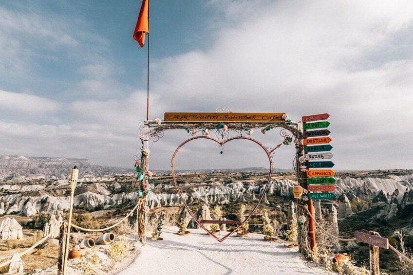A rustic archway with a heart-shaped top, surrounded by a metal fence and various signs pointing to different destinations. 4
