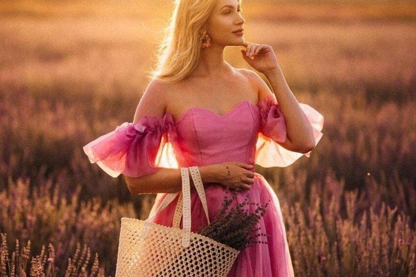 A person in a field with tall grasses, wearing a pink dress with ruffled sleeves, holding a woven bag. 5