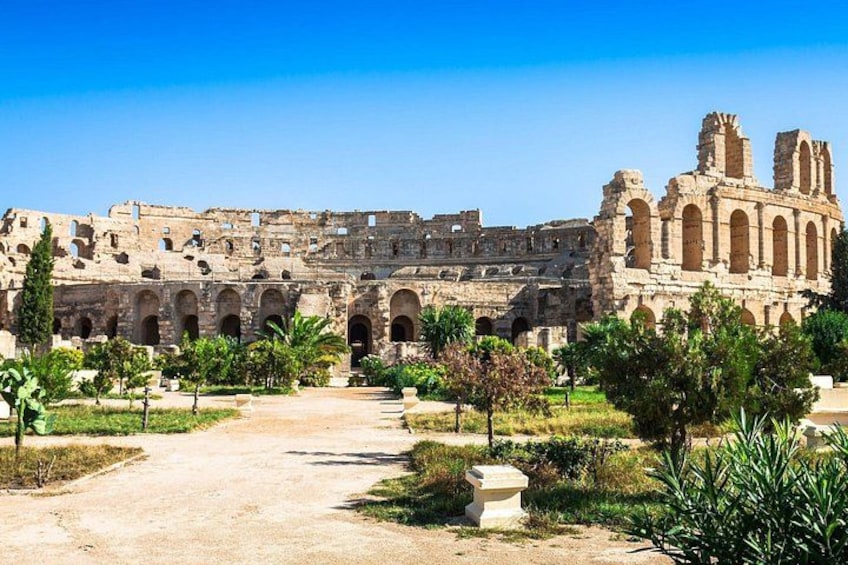 An ancient Roman amphitheater with arches and ruins, surrounded by greenery and a clear sky. 3