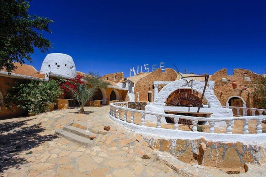 A historic building with a white dome and arches, a stone pathway, and a sign that reads 'MUSEE'. 2