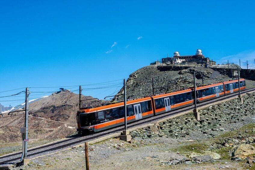 A train on tracks with a mountainous backdrop and a building with domes on a hill. 2