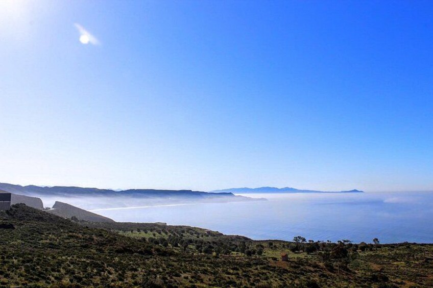 A coastal landscape with a clear sky, a distant mountain range, and a body of water. 2