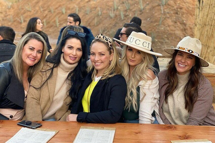 A group of people sitting at a wooden table outdoors with a desert landscape in the background. 5