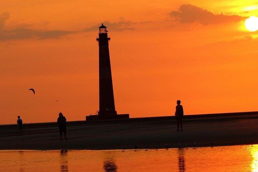 A lighthouse silhouette against a sunset sky, a beach with people, and a calm sea. 3