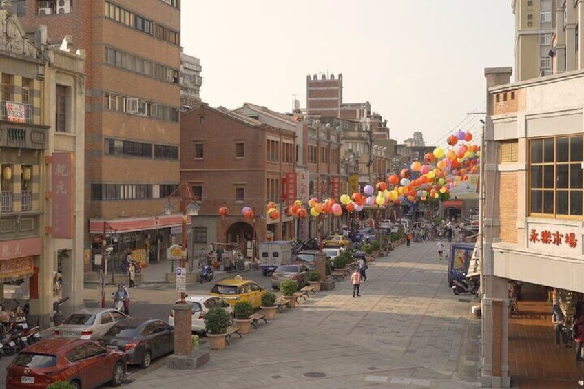 Une rue bordée d’immeubles, de voitures et d’une rangée de ballons aux couleurs vives. 2