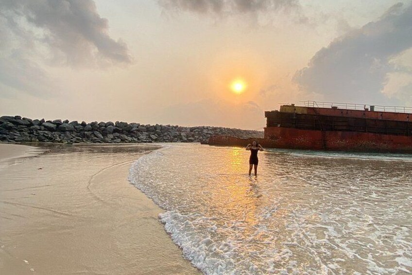 A beach with a person standing in the water, a sunset, and a large ship in the background. 5