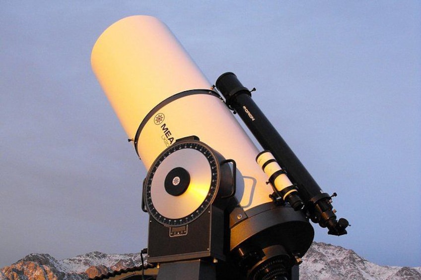 Un telescopio Meade con un ocular grande y una montura negra, sobre un fondo montañoso. 3